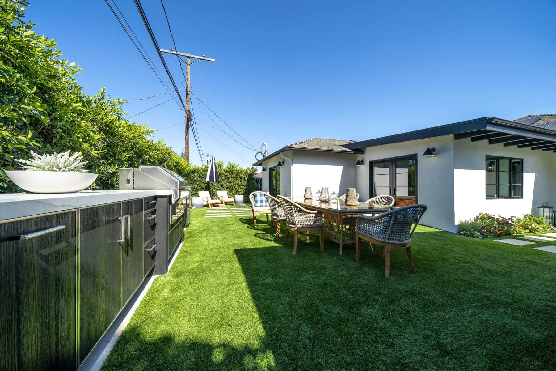 Outdoor dining area with a table, chairs, BBQ grill, and greenery