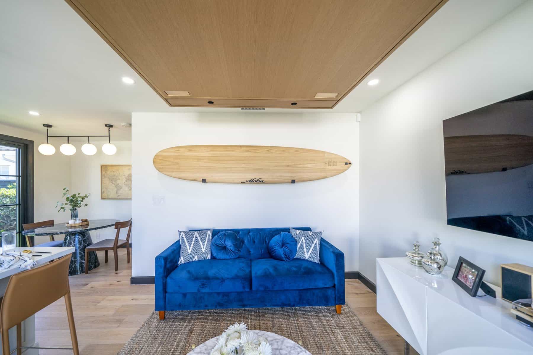 Cozy living area with blue velvet sofa, surfboard wall decor, and natural wood accents