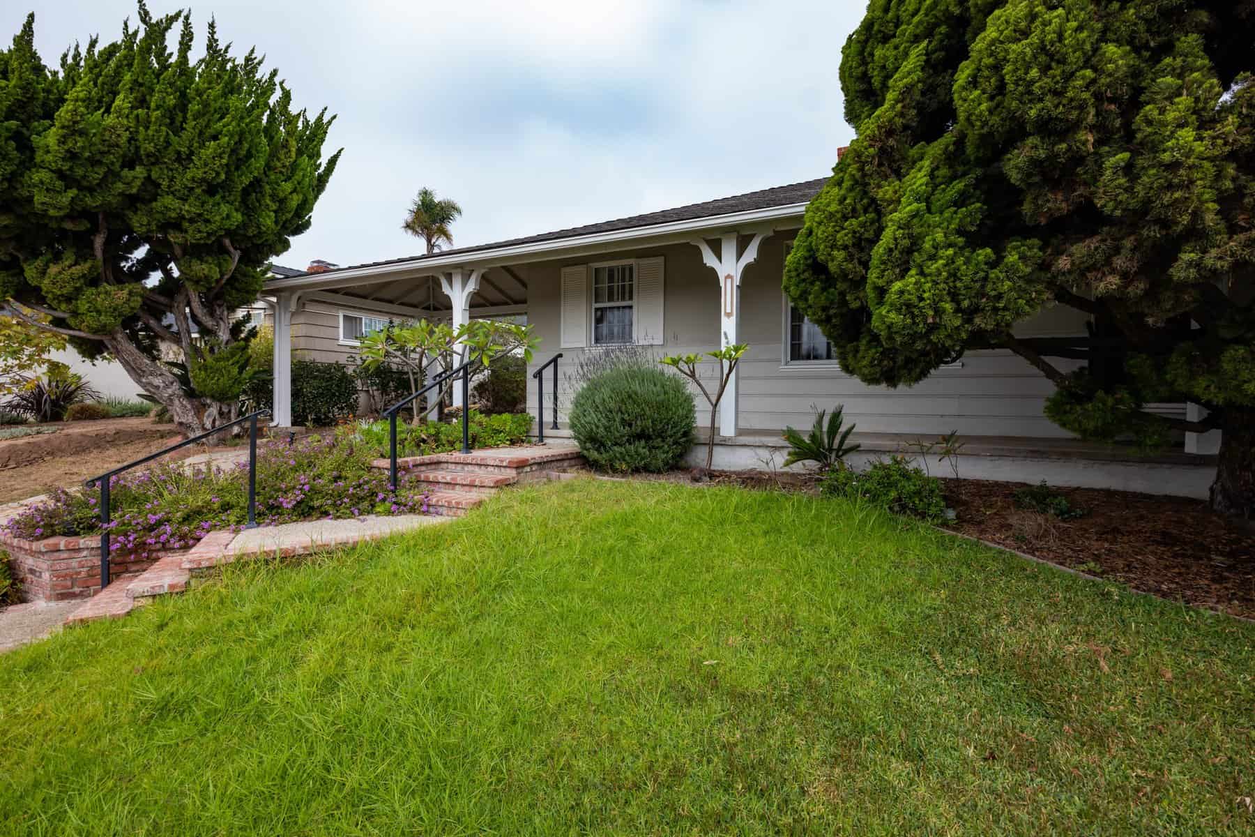 Single-story house with a front porch, brick steps, and well-maintained landscaping
