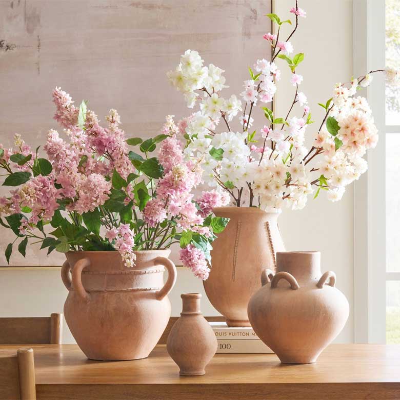 Terracotta vases filled with pink and white blooming flowers arranged on a wooden table.